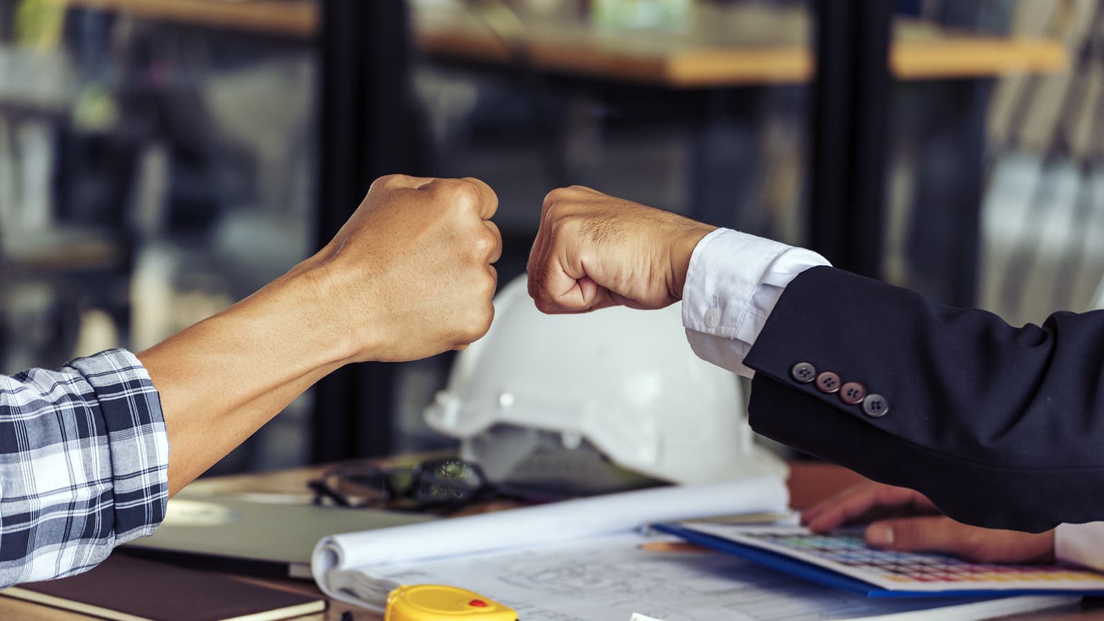 Two hands fist bump over commercial building plans