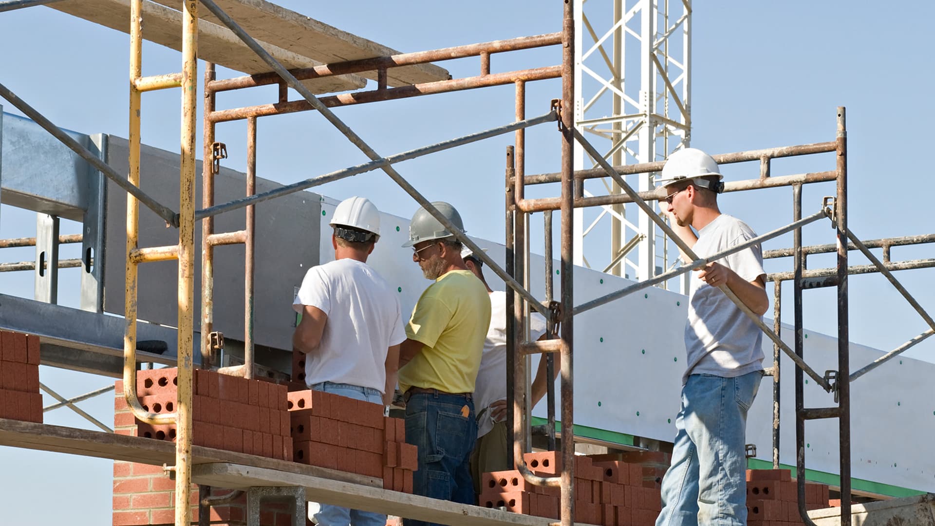 A crew of commercial builders work on a job site, discussing project around scaffolding
