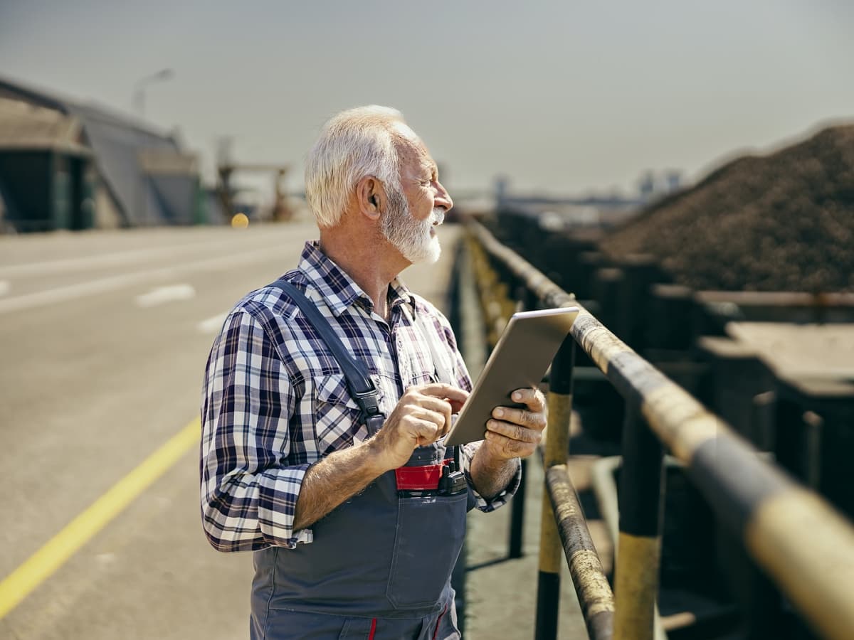 A senior man using a tablet while supervising construction project.