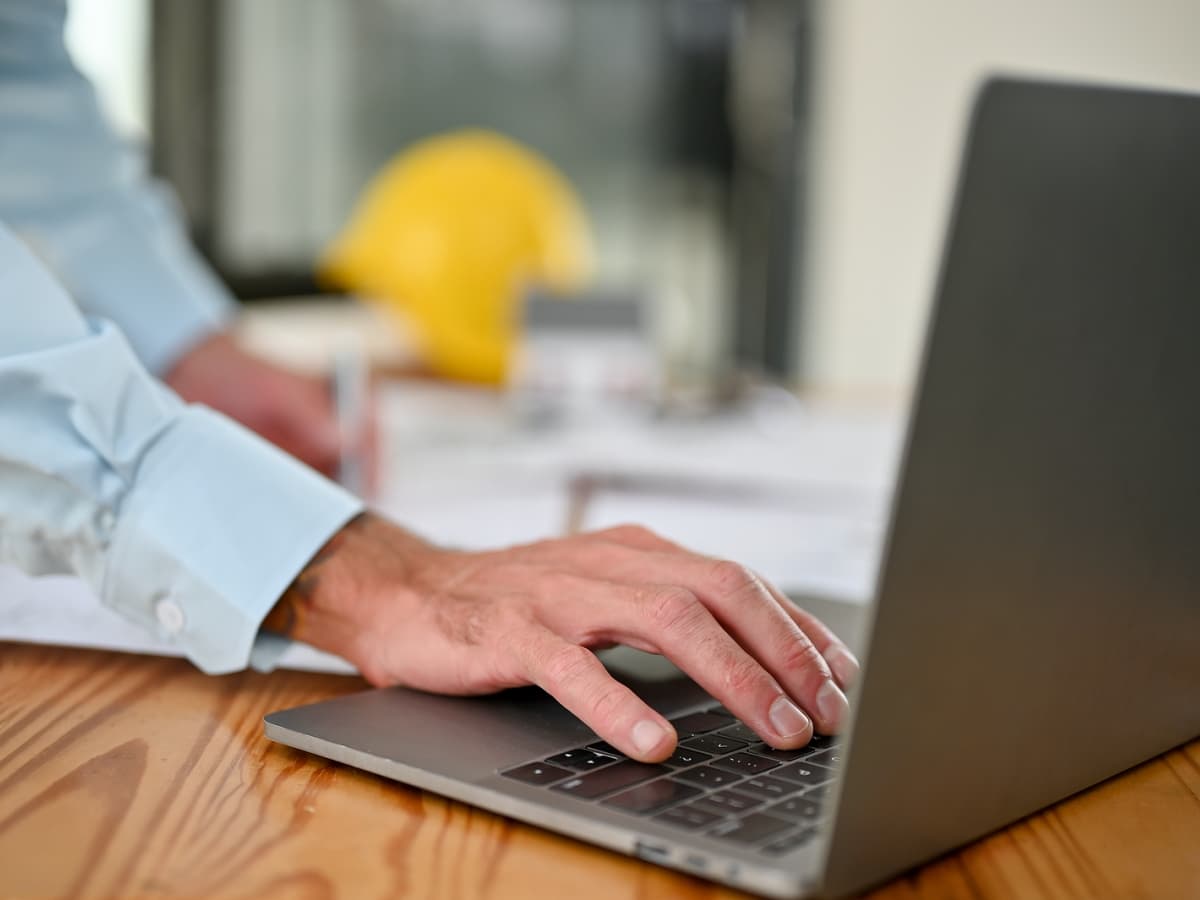 A construction manager typing on a laptop computer, focused and engaged in their work.