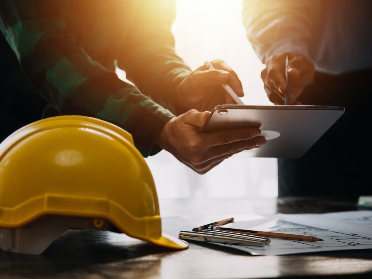 Two managers in hard hats working on a tablet, collaborating on a construction project.
