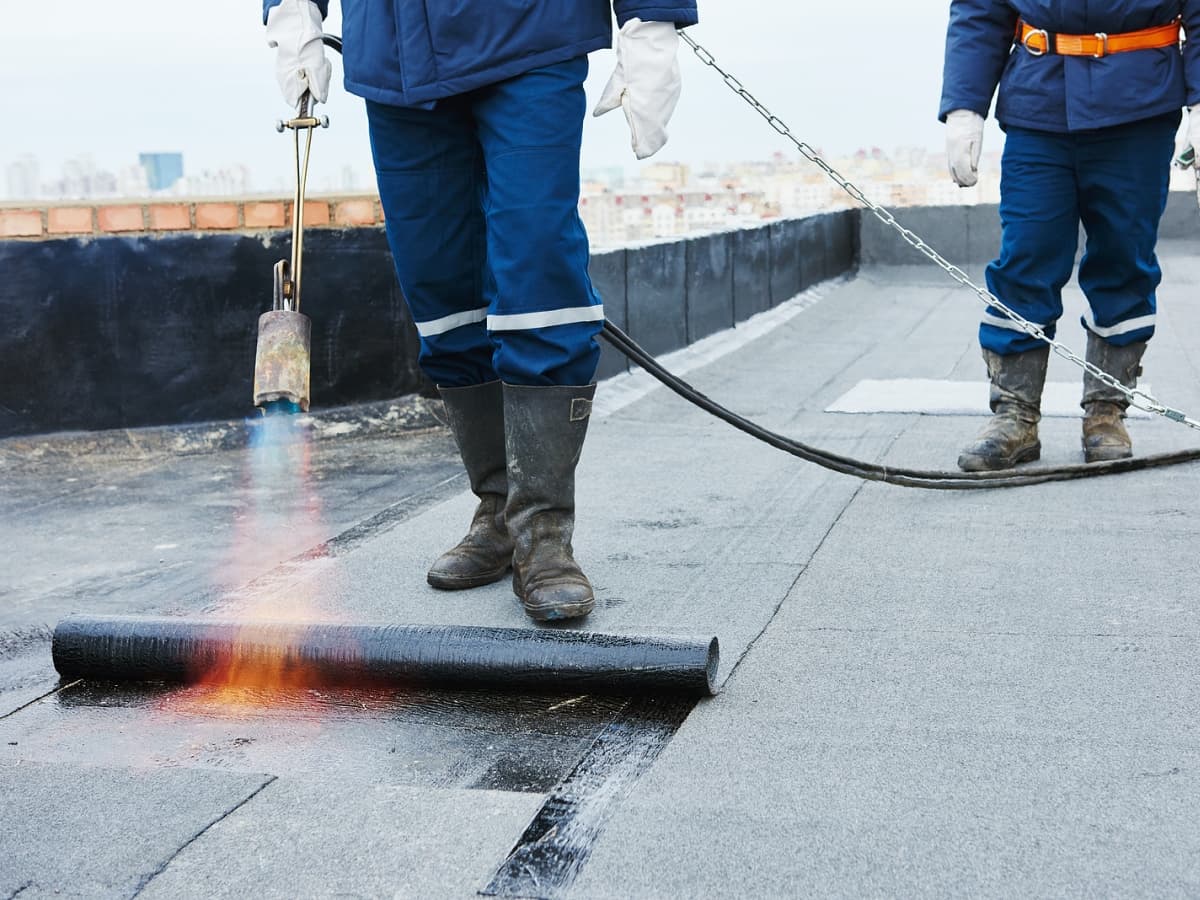 Roofers in blue overalls using a torch to treat roof.