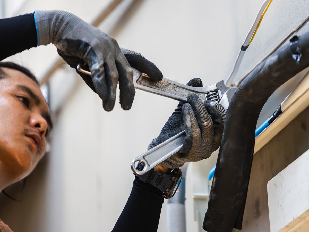 A person using a wrench-like tool on an object. The person is wearing gloves.