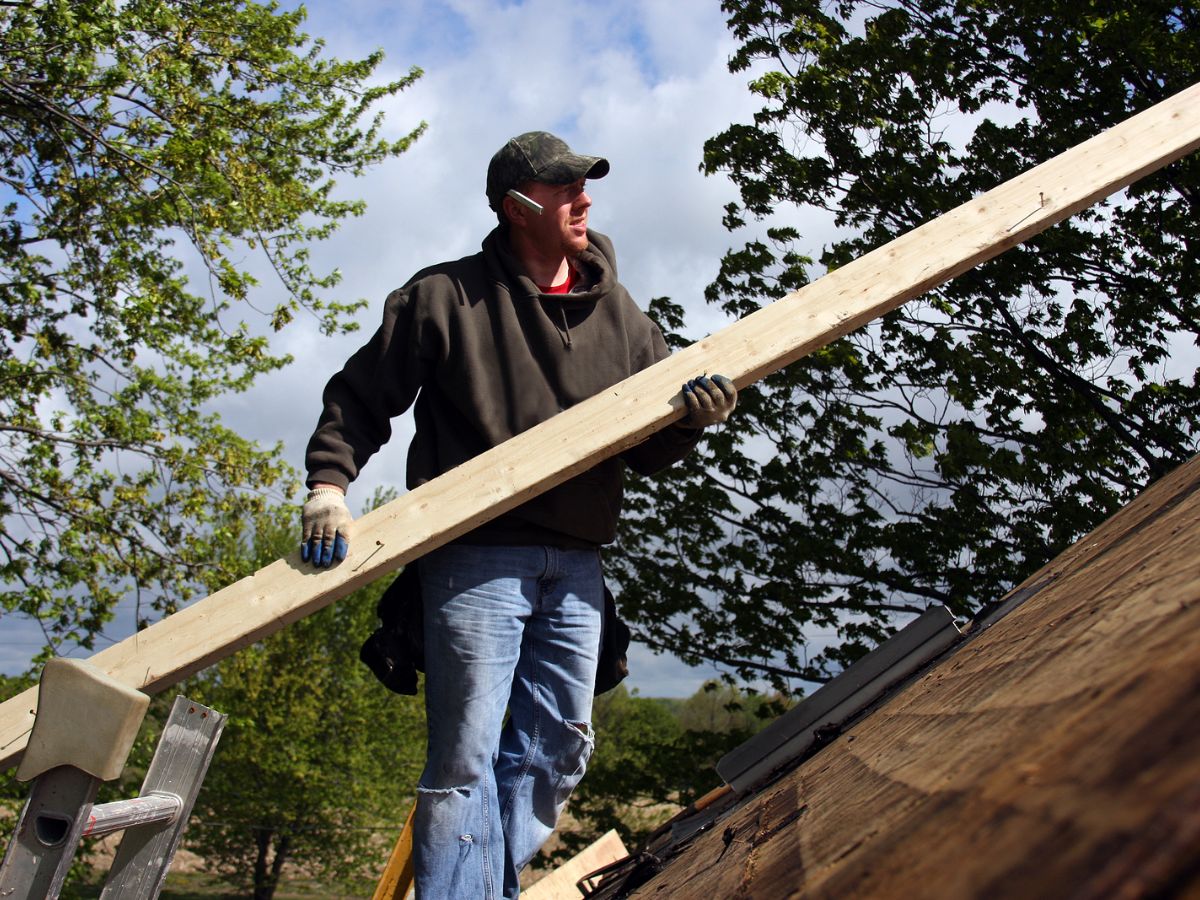 Person on a roof carrying a beam