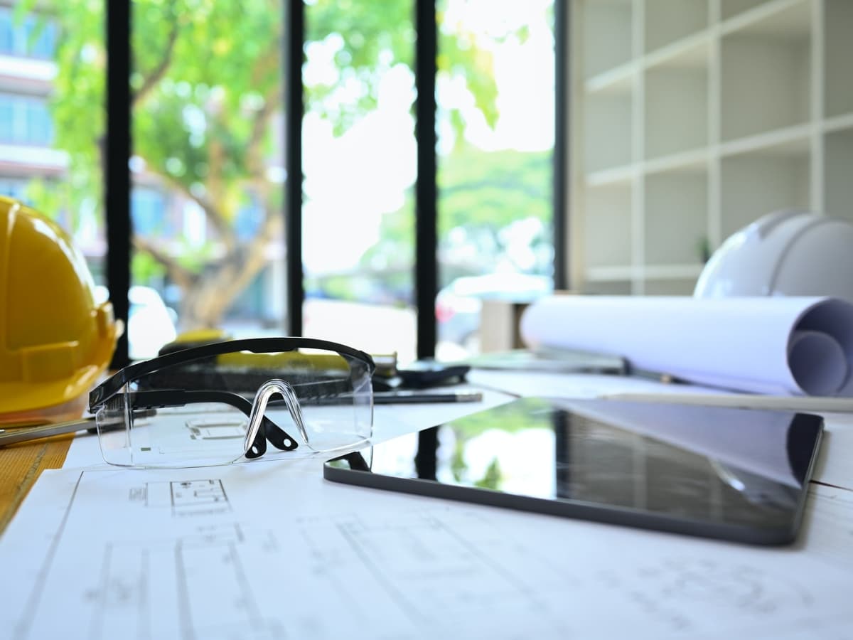 Work essentials on desk: hard hat, glasses, and tablet.