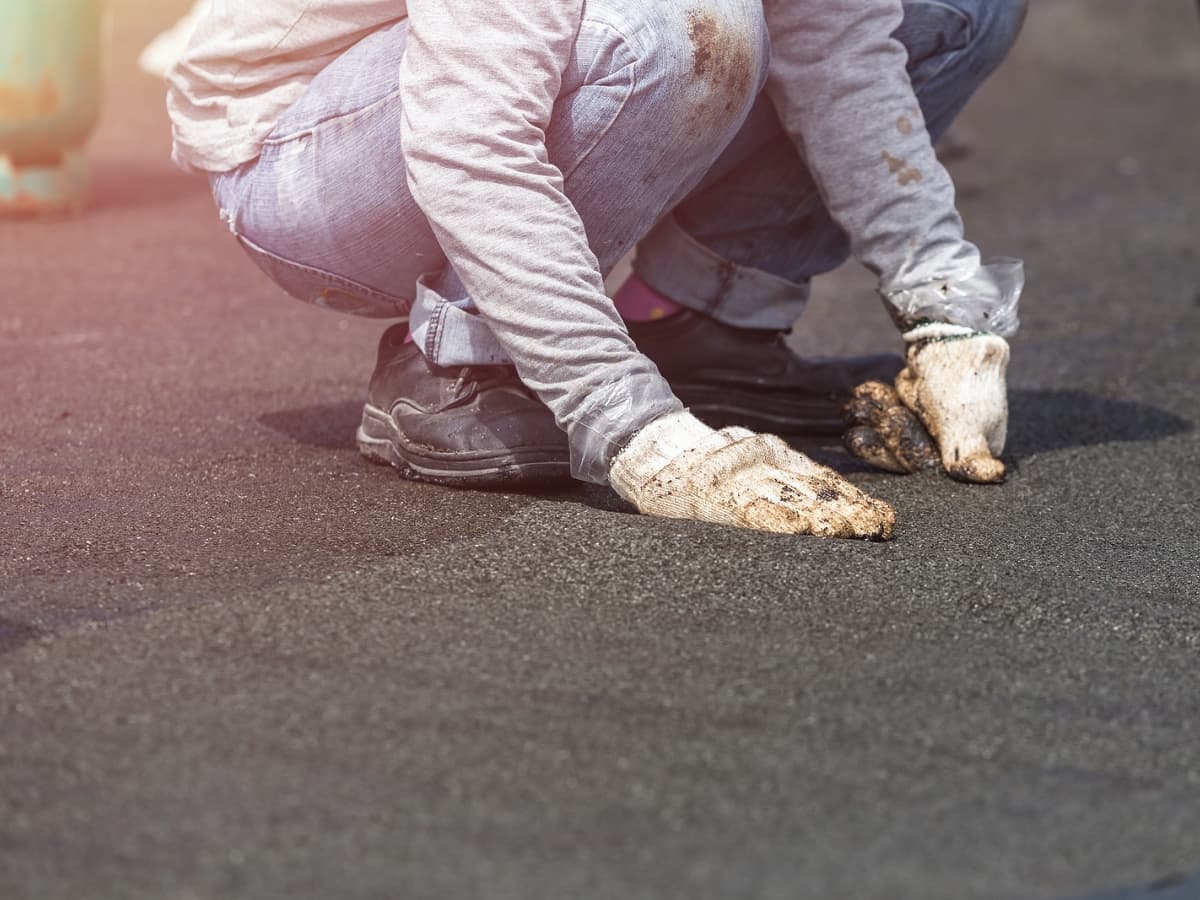 Roofer kneeling on the ground, his hands resting on the asphalt.