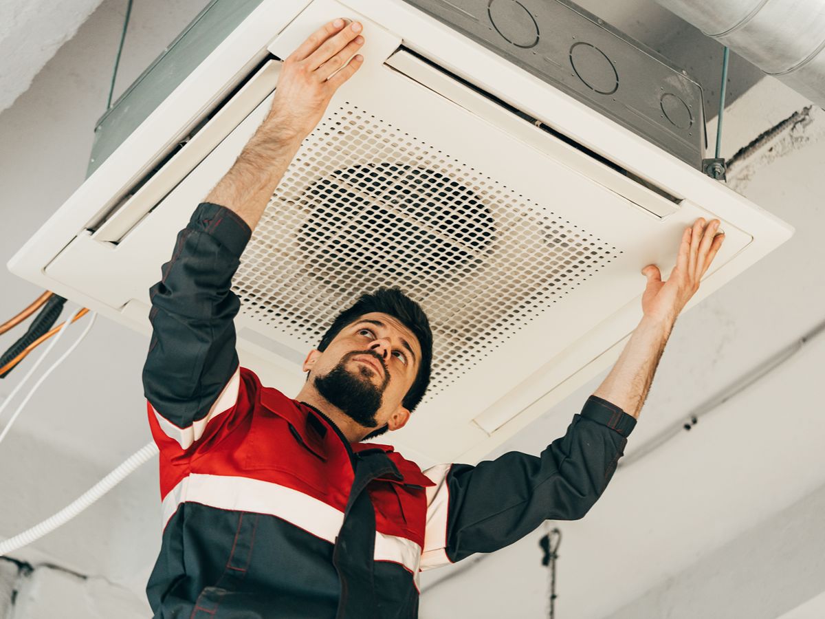 A person doing work on some equipment that is hanging from the ceiling.